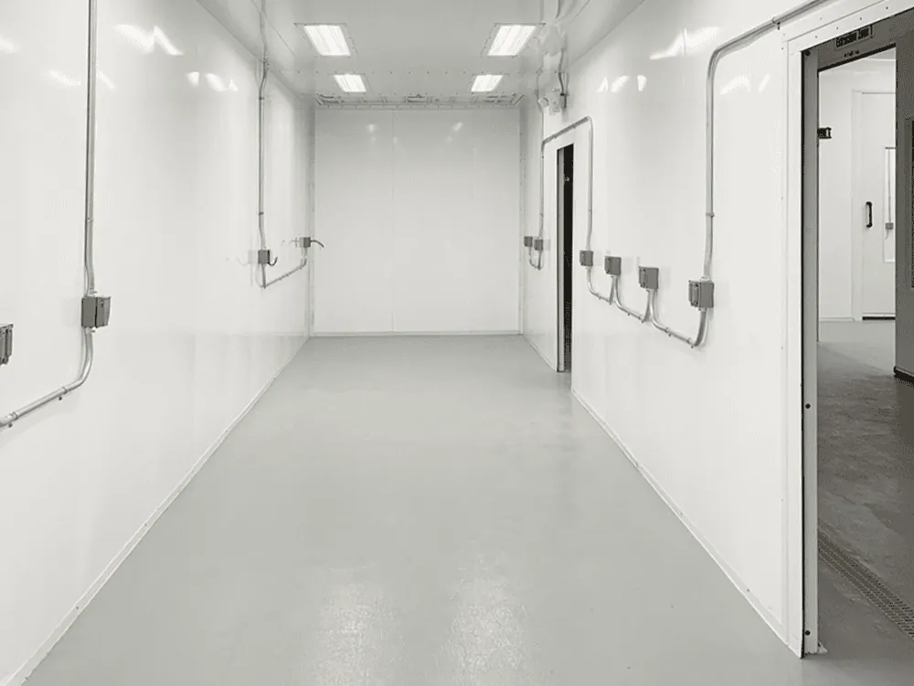 Interior corridor of a multi-zone enclosure showing flush epoxy floor, integrated electrical drops, and overhead LED lighting.